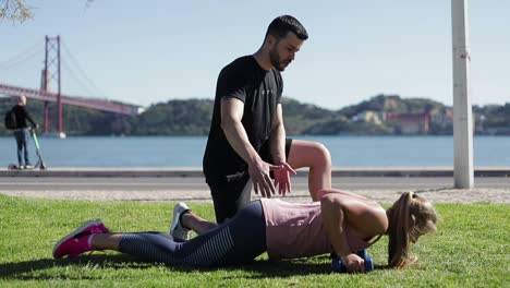 Side-view-of-young-woman-doing-push-ups-with-dumbbells-in-park.